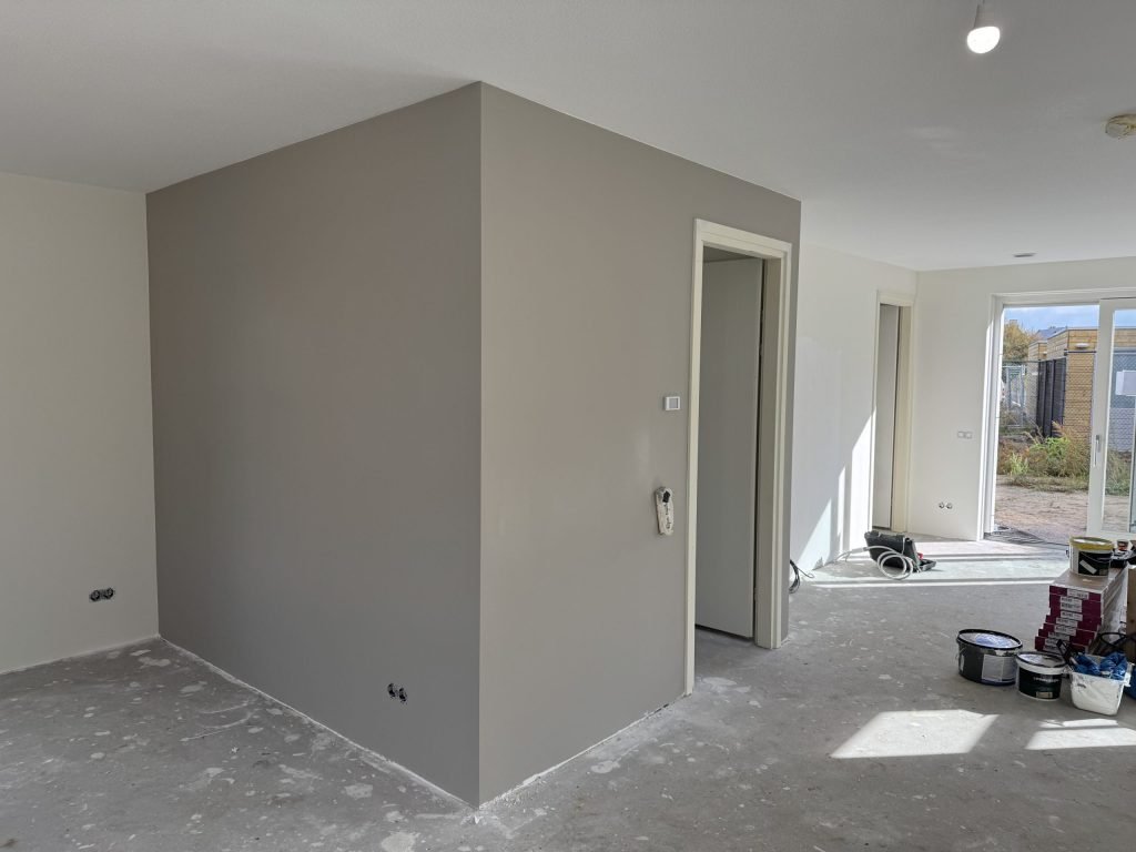 Pas afgewerkte grijze wand in een woning, met verfemmers op de vloer